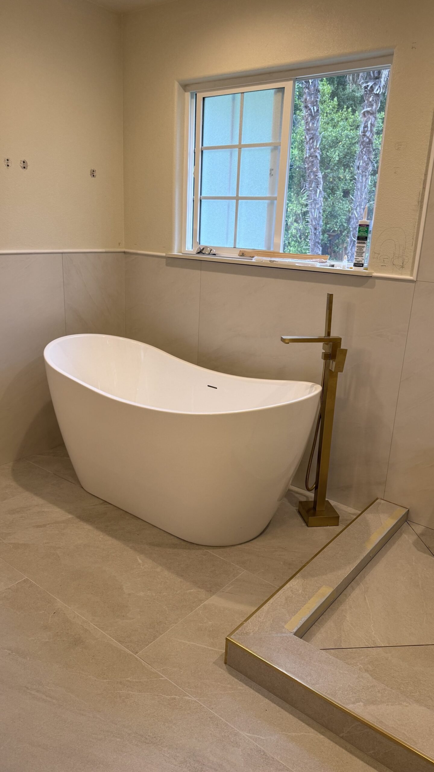 Freestanding soaking tub with brushed gold floor-mount filler mid-remodel, before the shower glass was installed