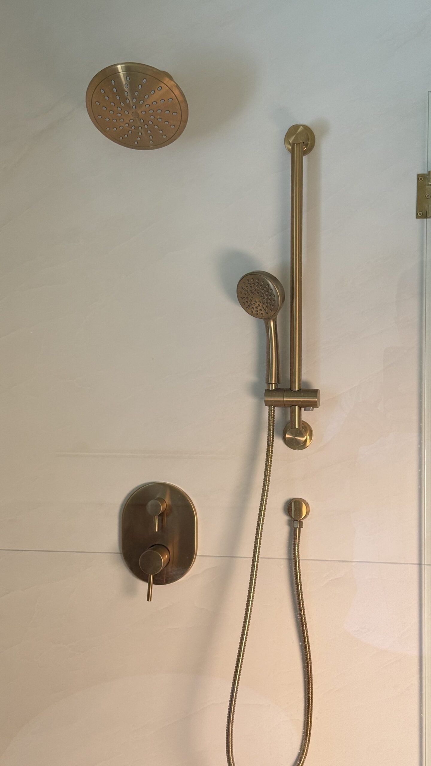 Detail of the rain shower head, slide-bar handheld, and valve trim in brushed gold