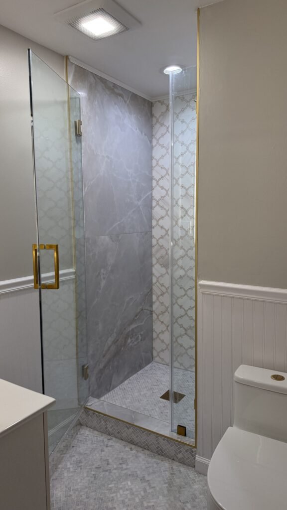 Finished corner glass shower with hand-set arabesque mosaic accent wall and herringbone floor