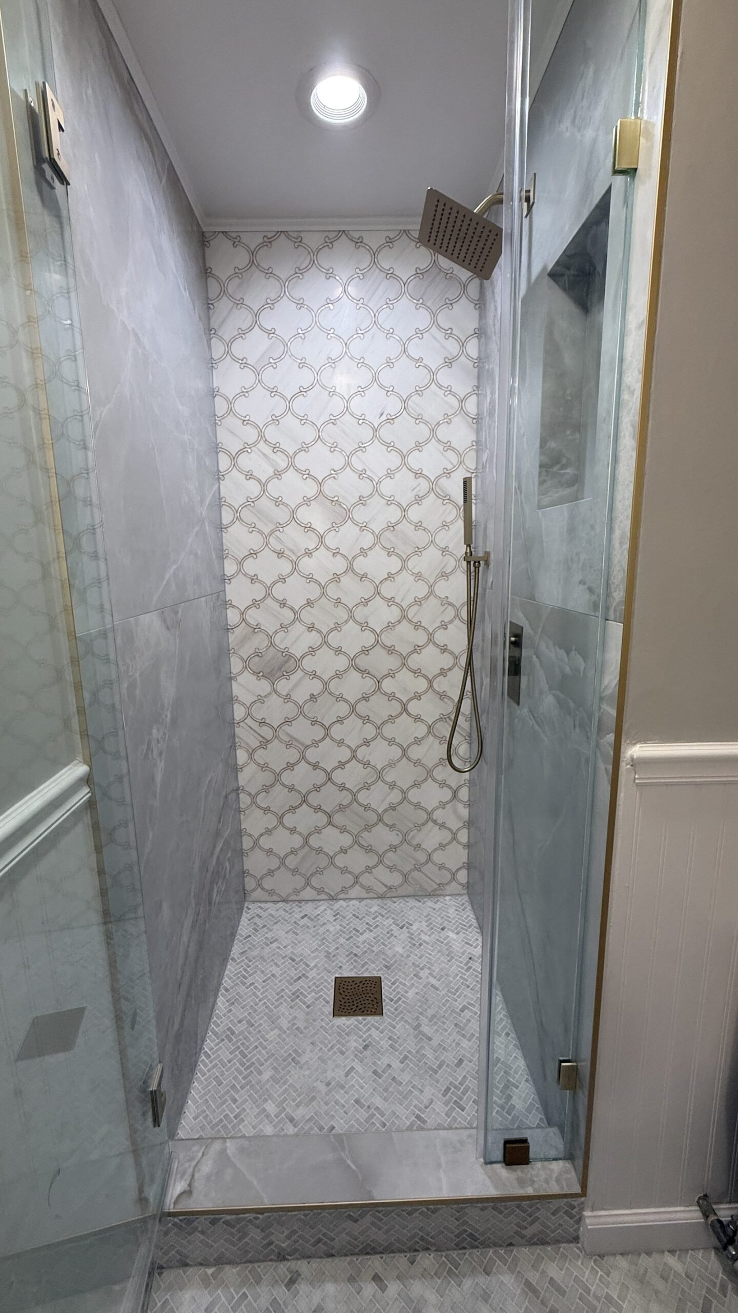Shower interior with arabesque mosaic accent wall, handheld sprayer, and floor drain
