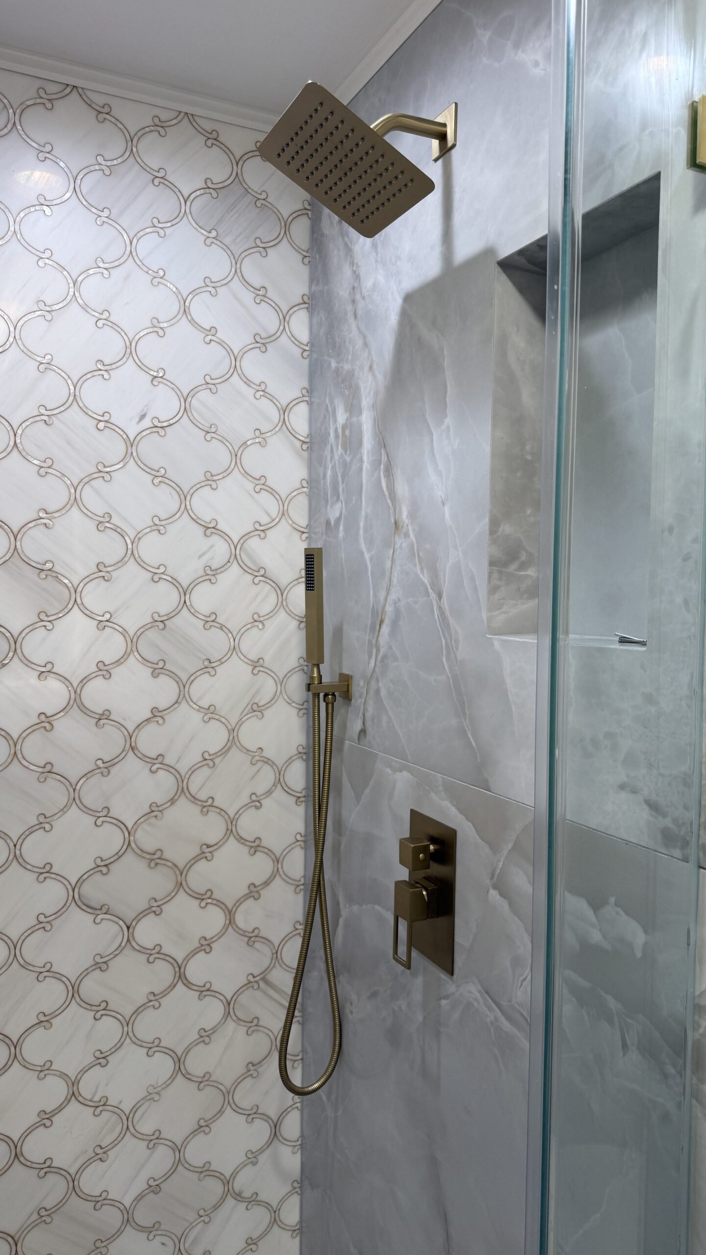 Detail of brushed gold showerhead, handheld sprayer, and valve trim against arabesque mosaic tile